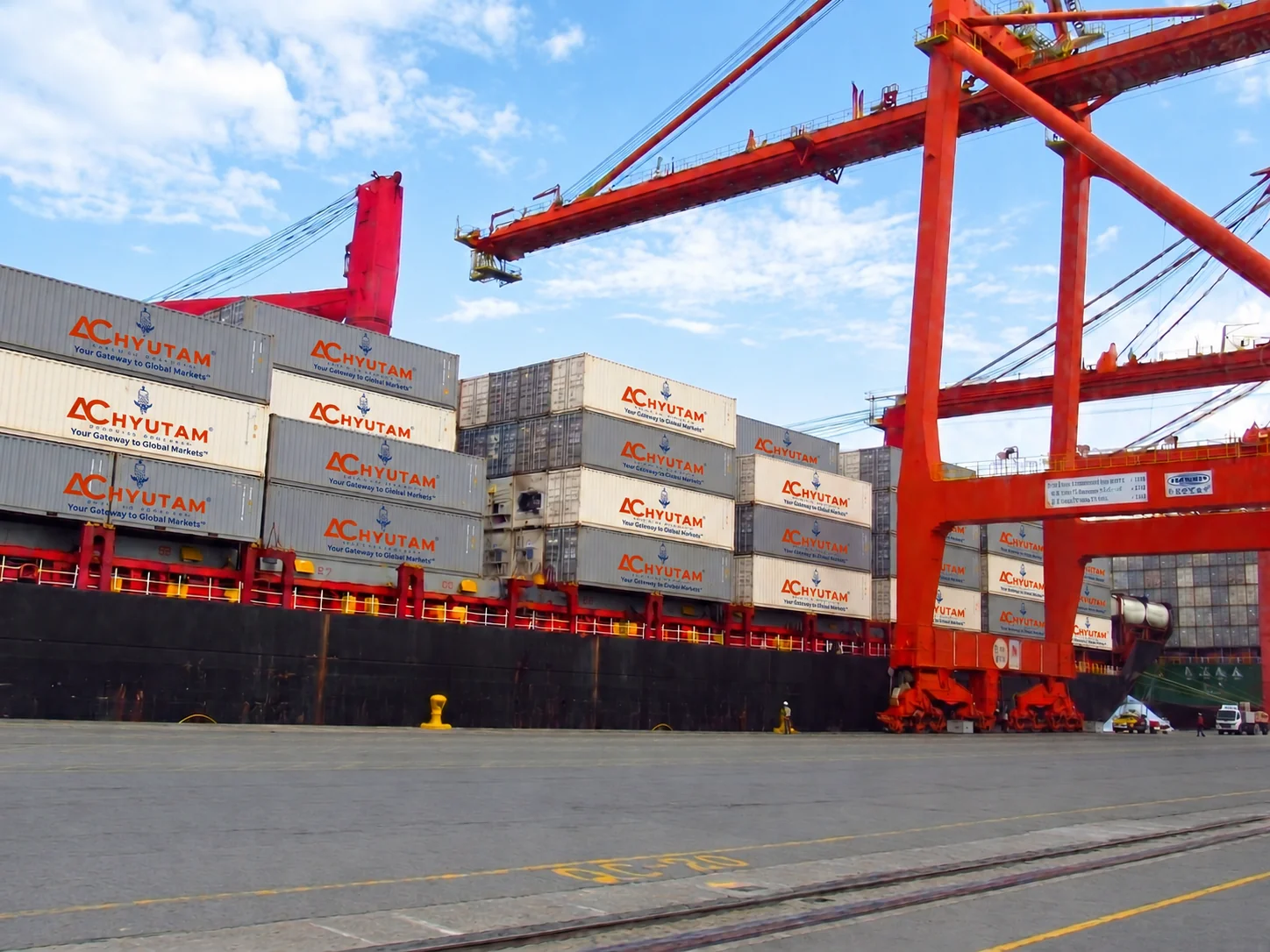 ACHYUTAM branded shipping containers being loaded by a gantry crane at a container terminal