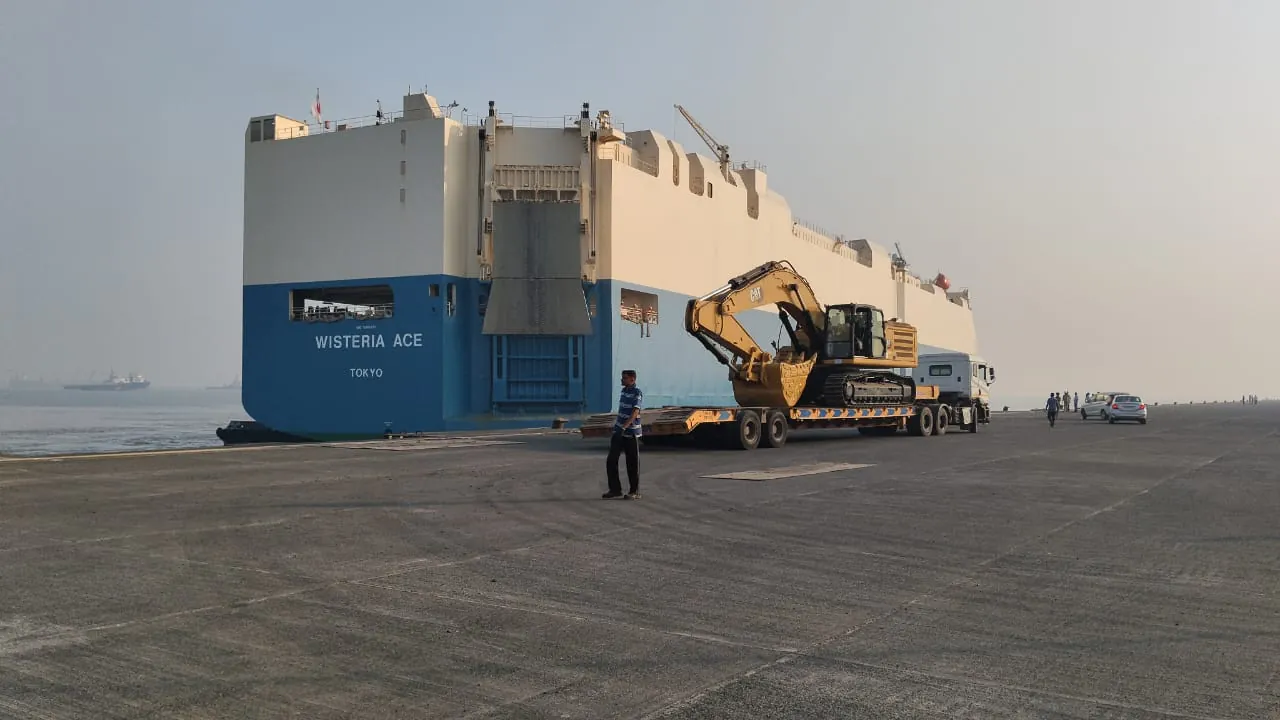 Excavator on a low-bed trailer beside a vessel at the port