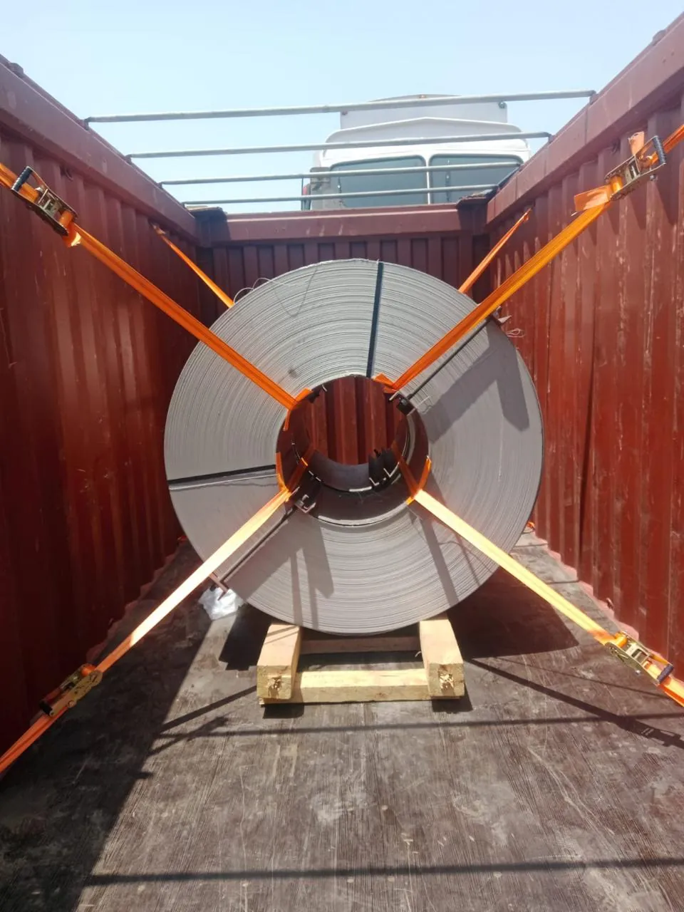 Steel coil secured with lashing straps inside an open-top container