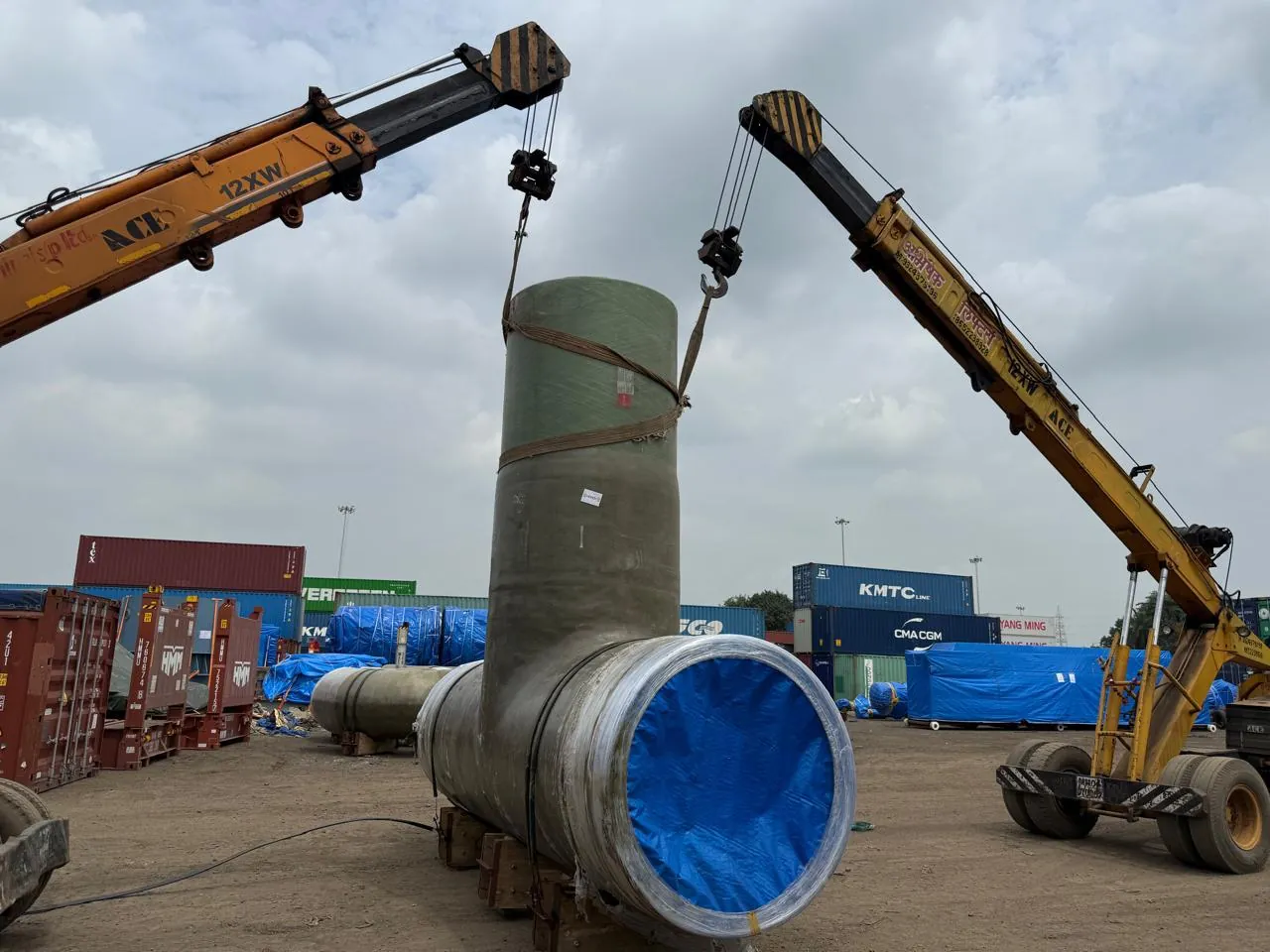 Large fibreglass pipe lifted by two cranes in a container yard