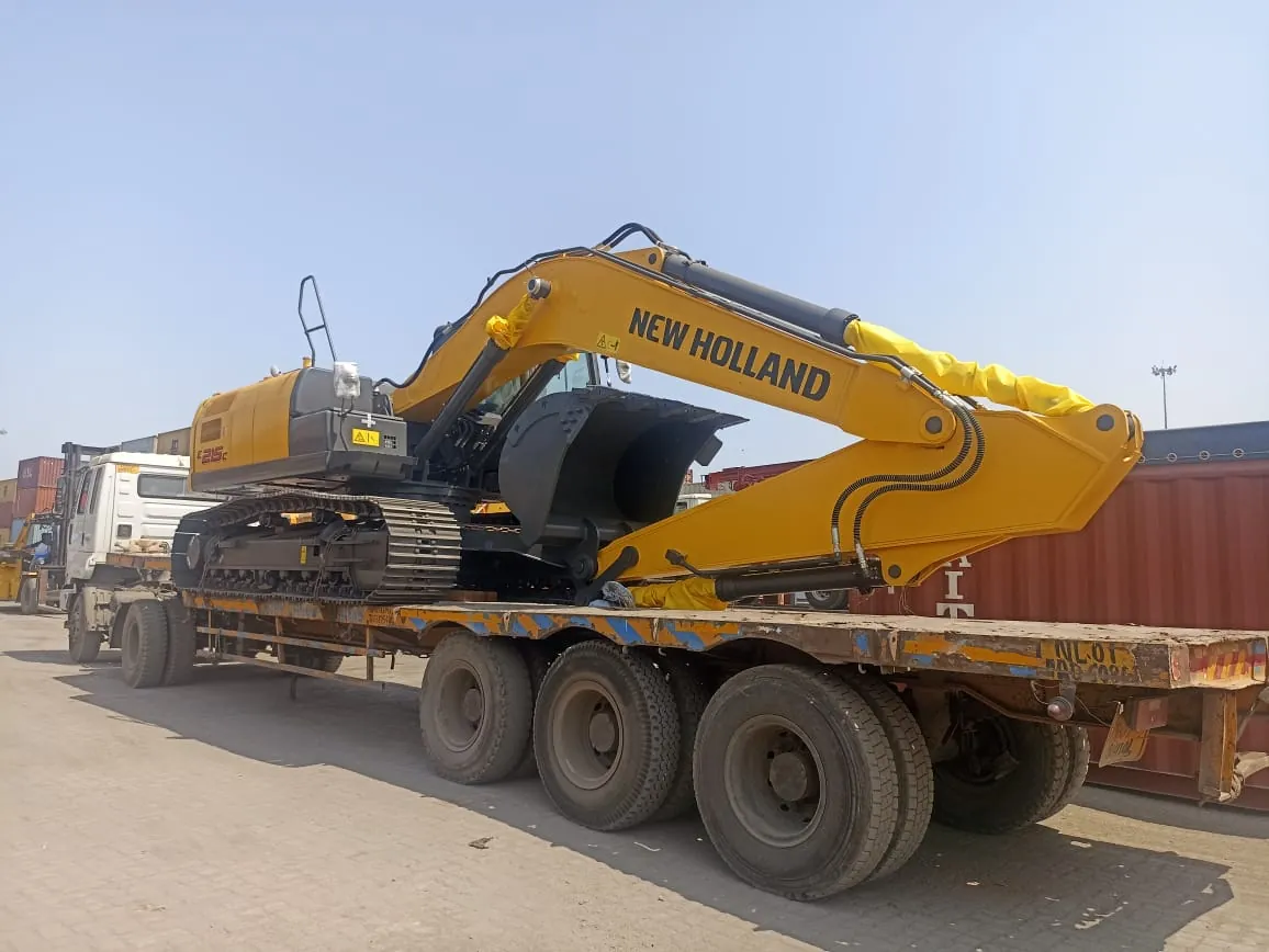 New Holland excavator loaded on a low-bed trailer in a container yard