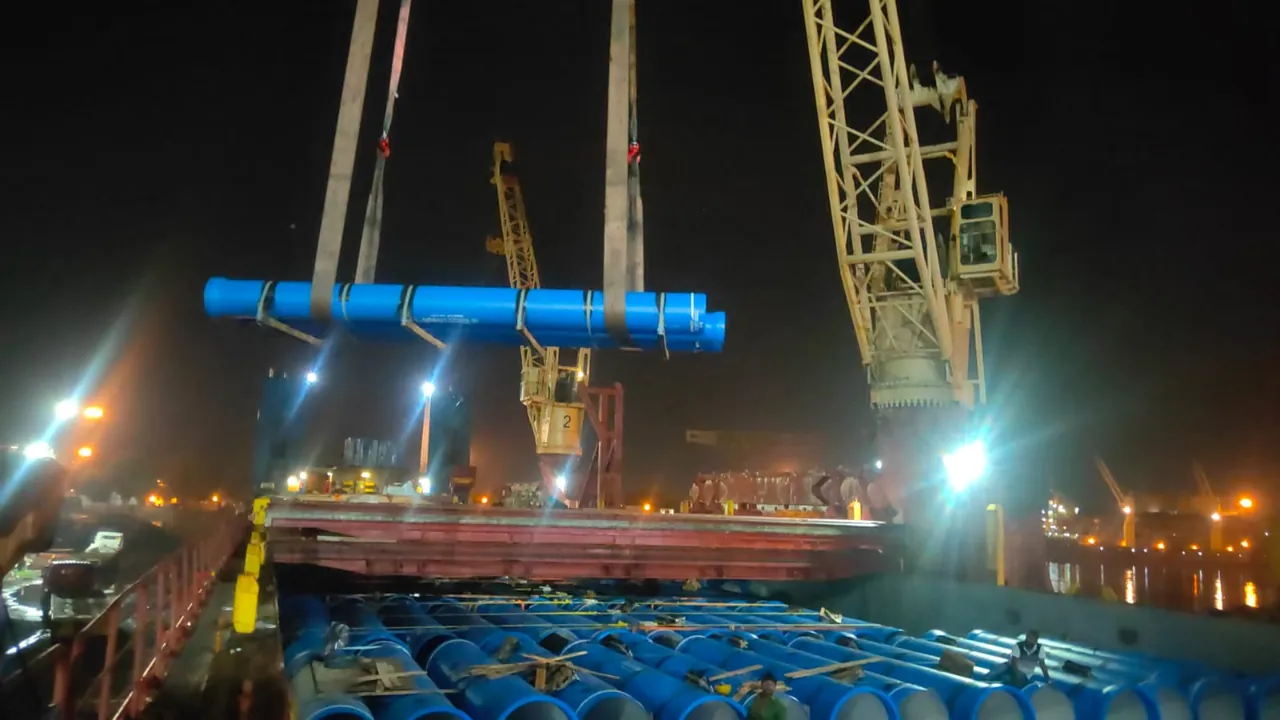 Bundle of blue pipes lifted by crane at the port at night